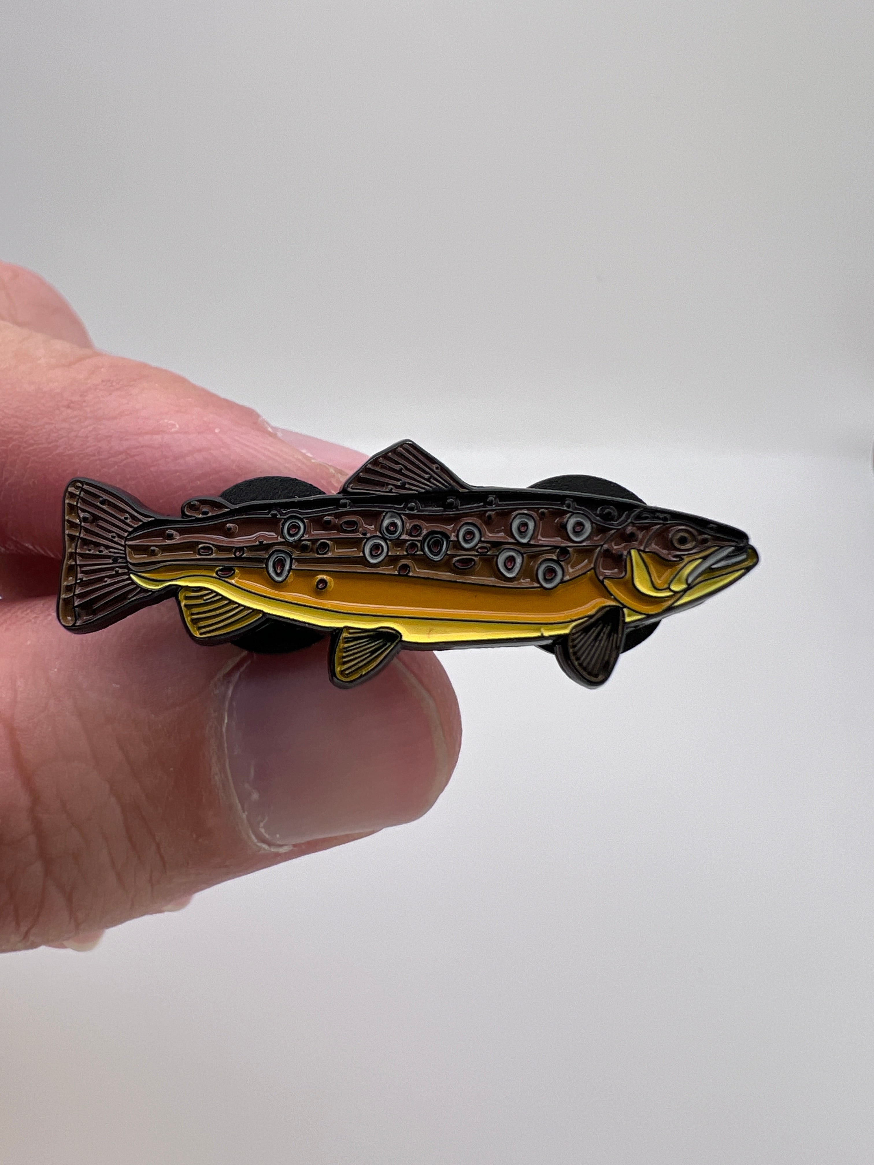 Gold and black fish-shaped object held between fingers against a white background