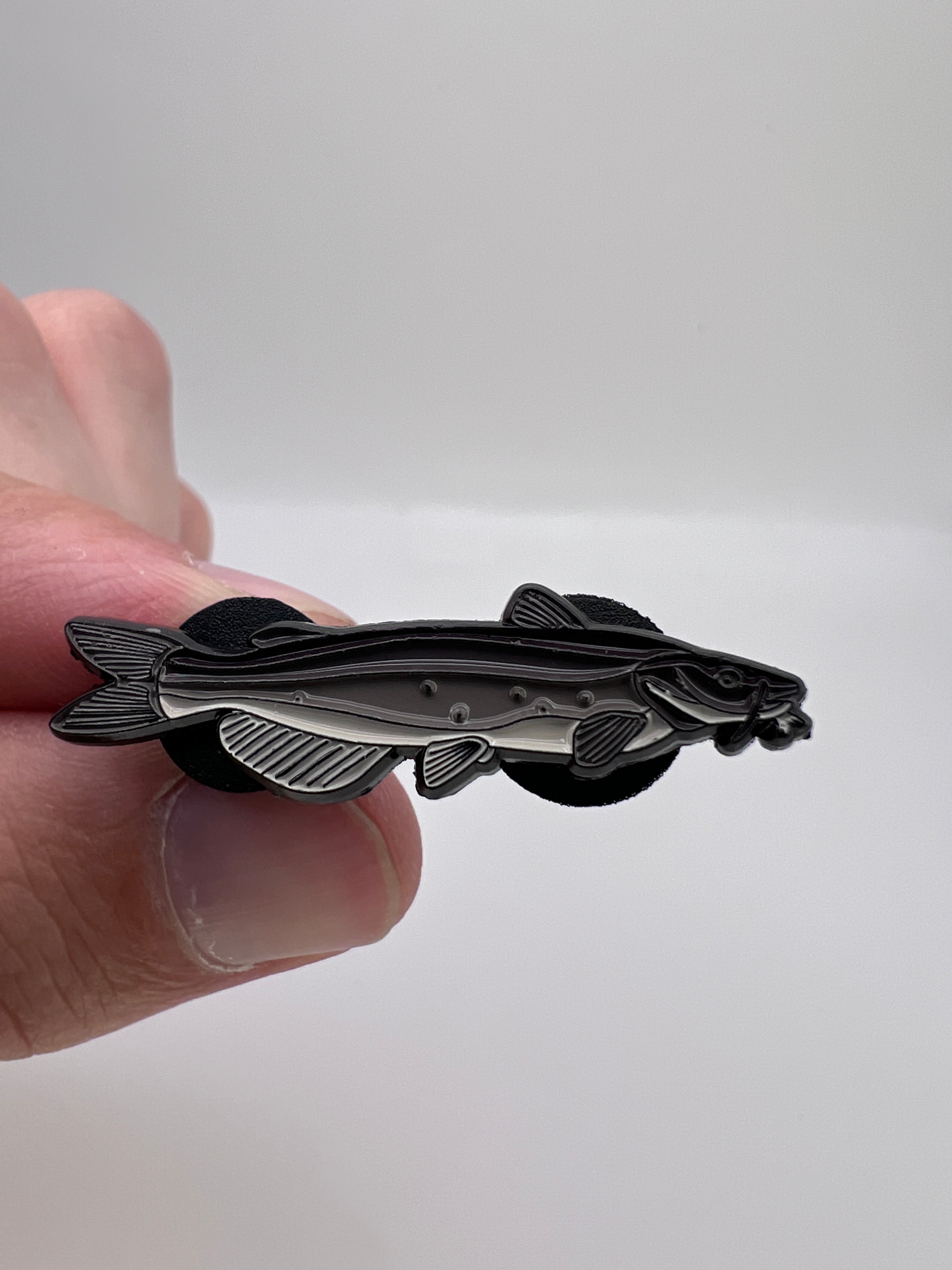 Hand holding a silver fish-shaped pin against a white background
