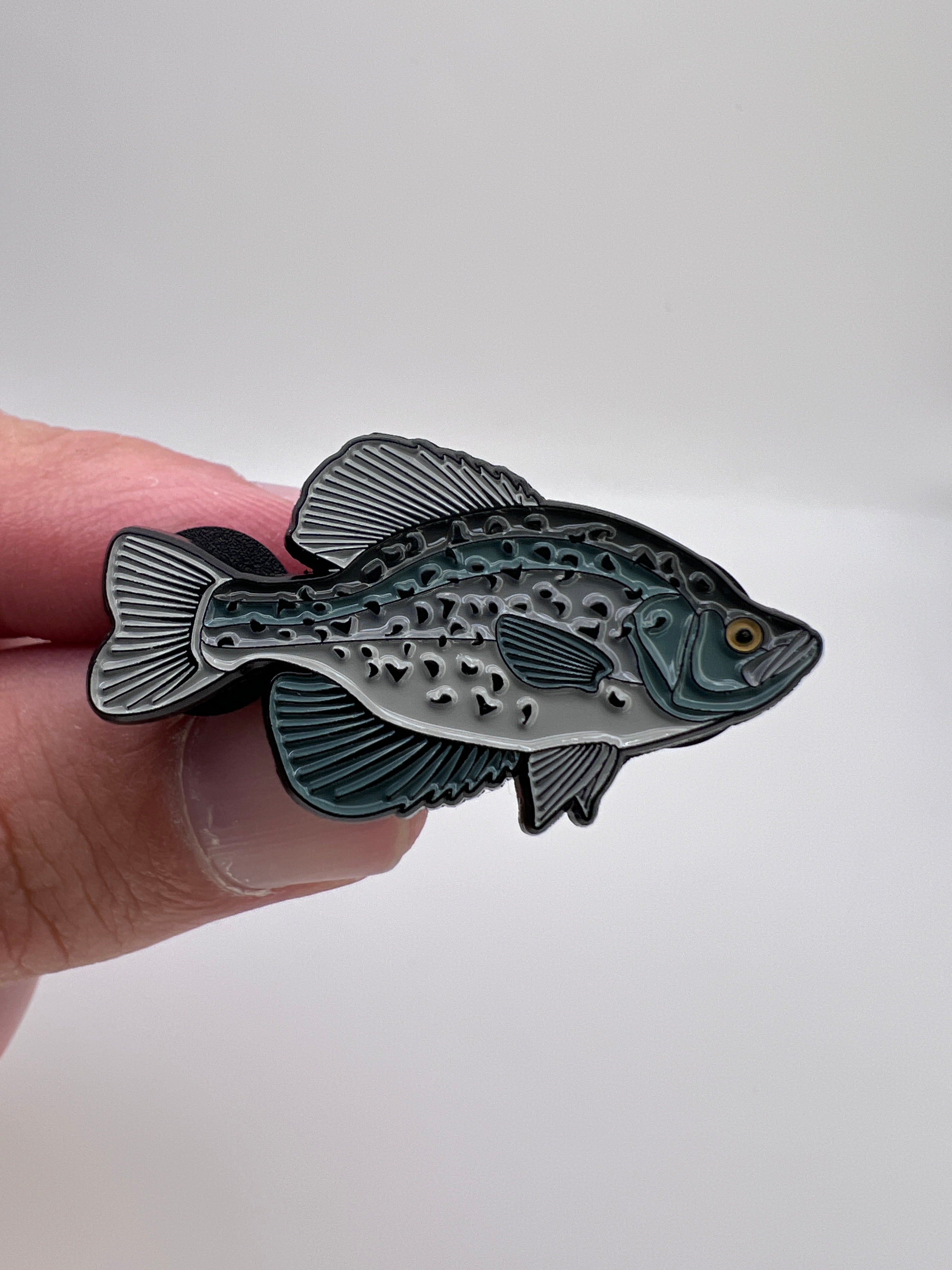Fish-shaped metal badge held between fingers against a white background
