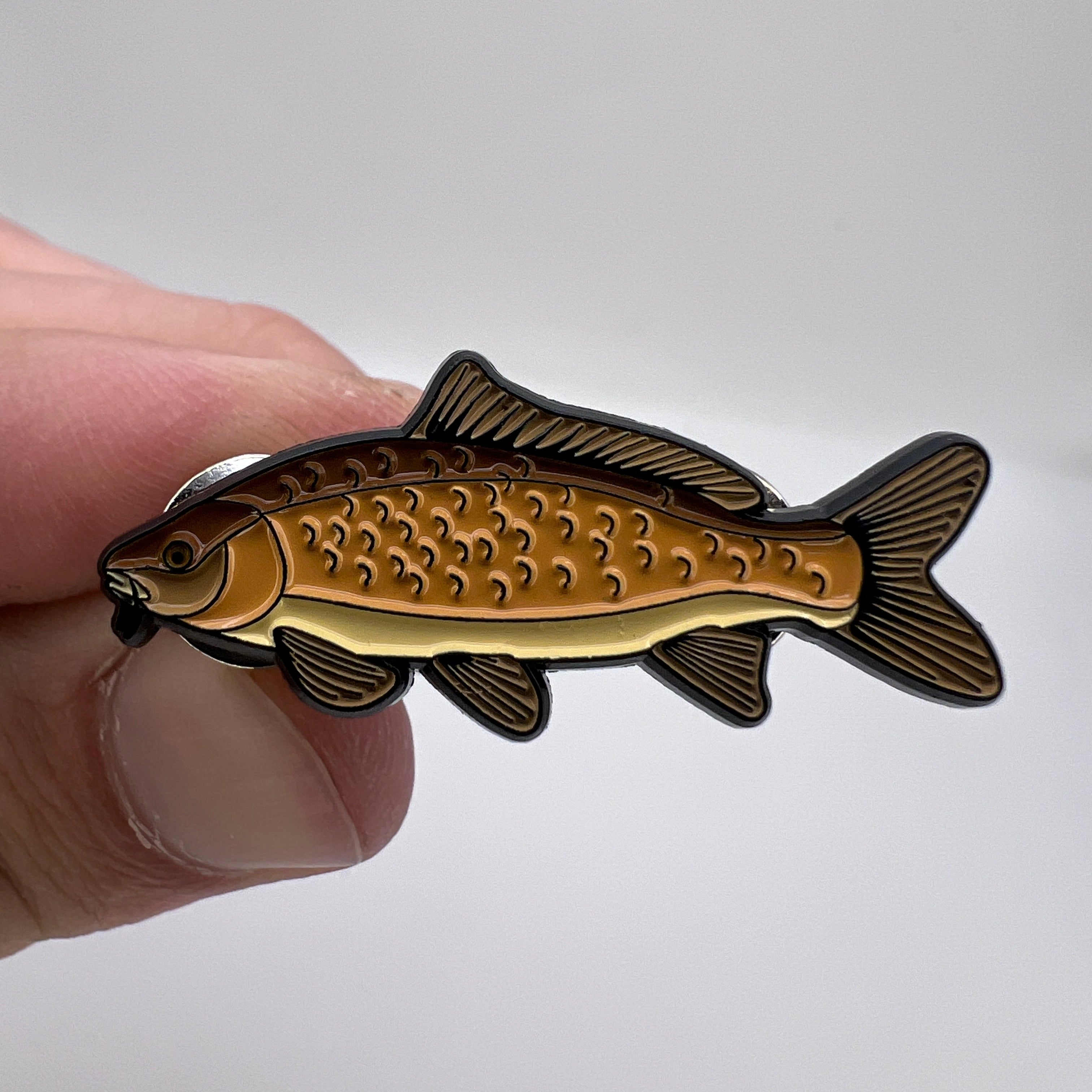 Gold and black fish-shaped pin held by a hand against a white background