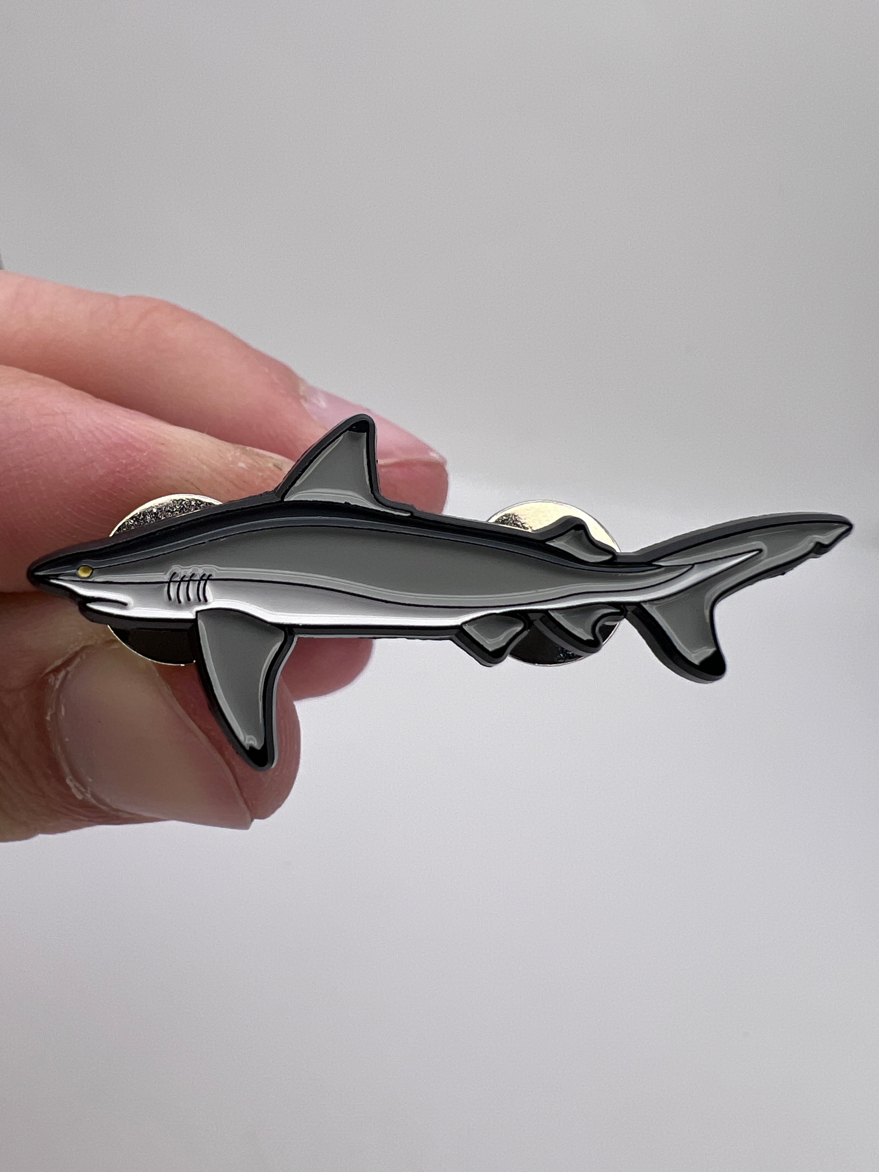 Shark-shaped metal badge held in a hand against a plain background