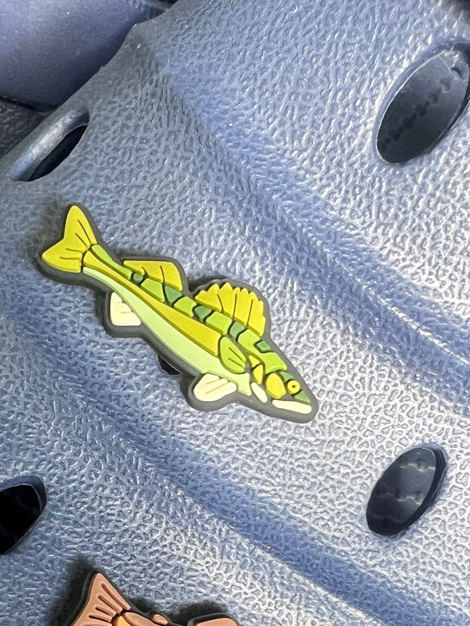 fish-shaped charm on a blue sandal with grass in the background