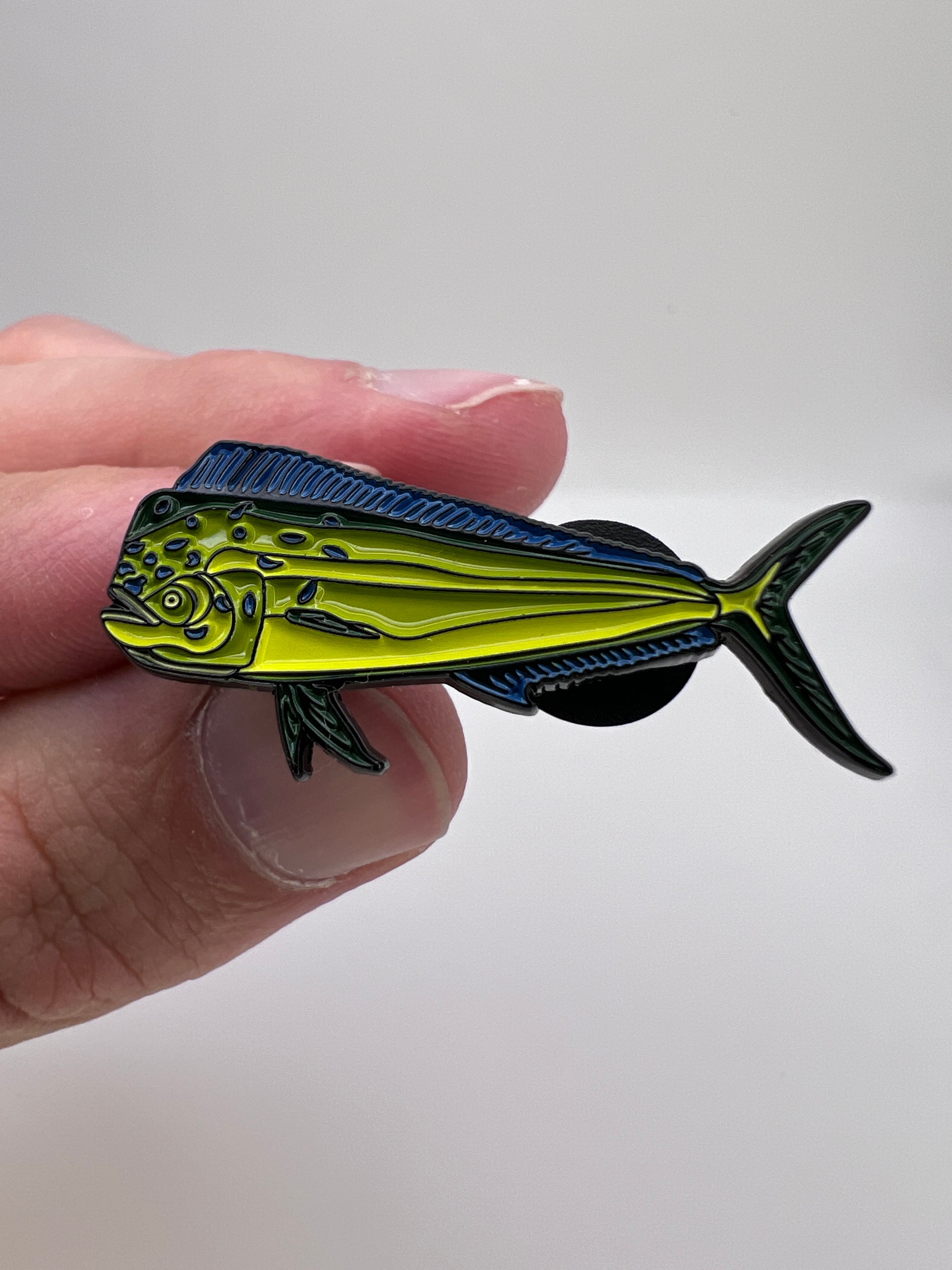 Hand holding a yellow and black fish-shaped pin against a white background