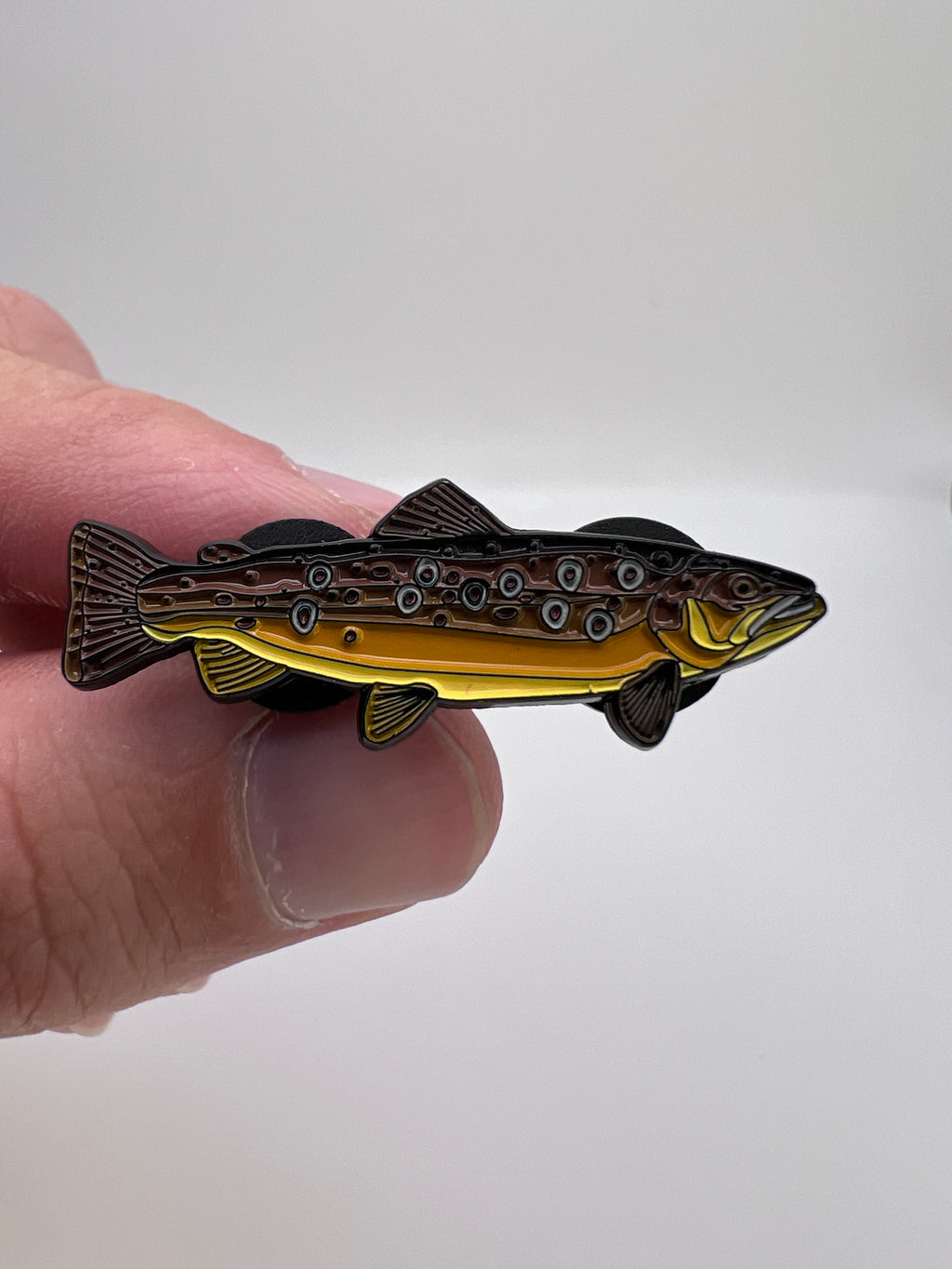 Gold and black fish-shaped object held between fingers against a white background