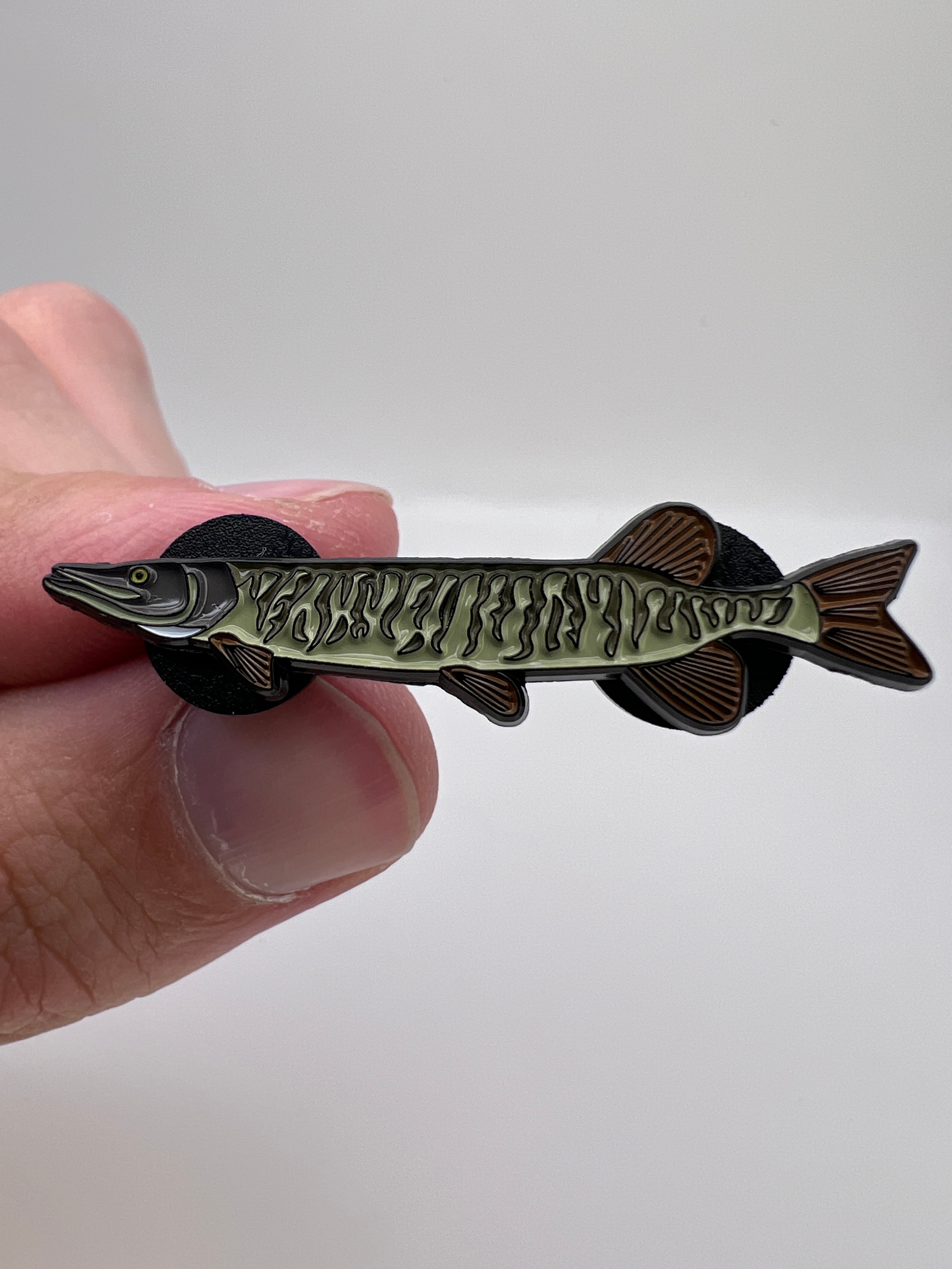 Fishing lure shaped like a fish held between fingers against a white background
