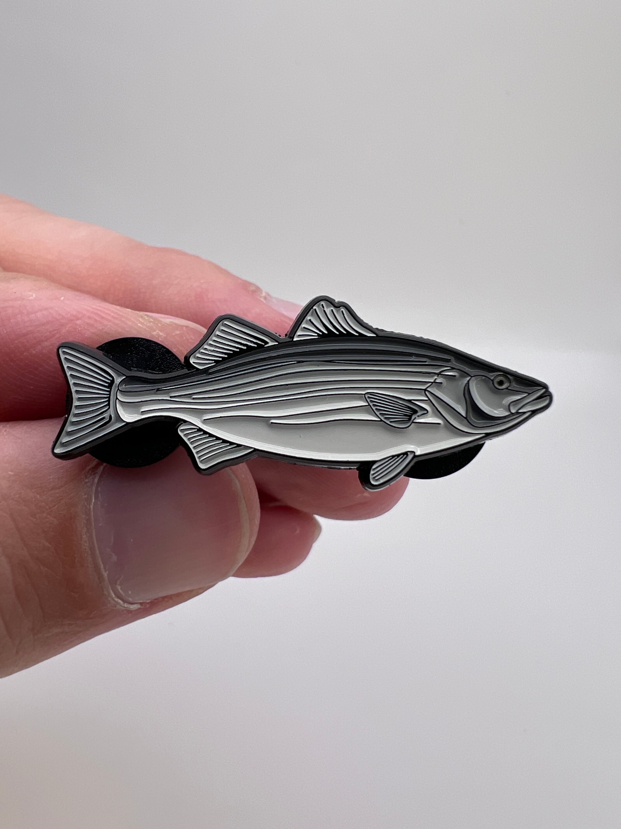 Hand holding a fish-shaped metal badge against a white background