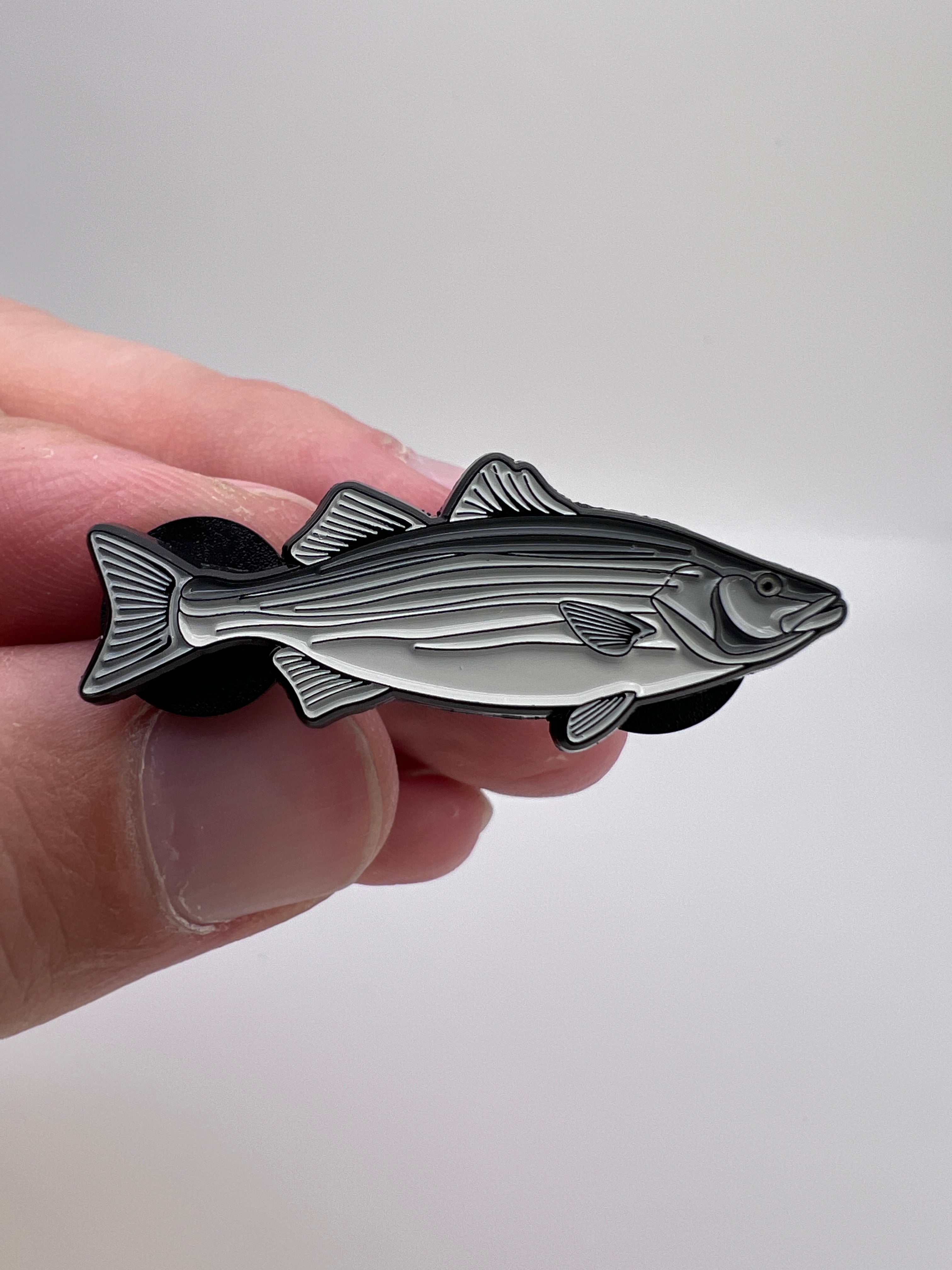Hand holding a fish-shaped metal badge against a white background