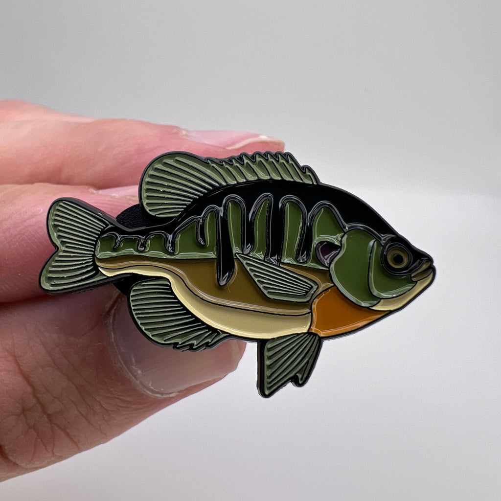 Fish-shaped pin held between fingers against a white background