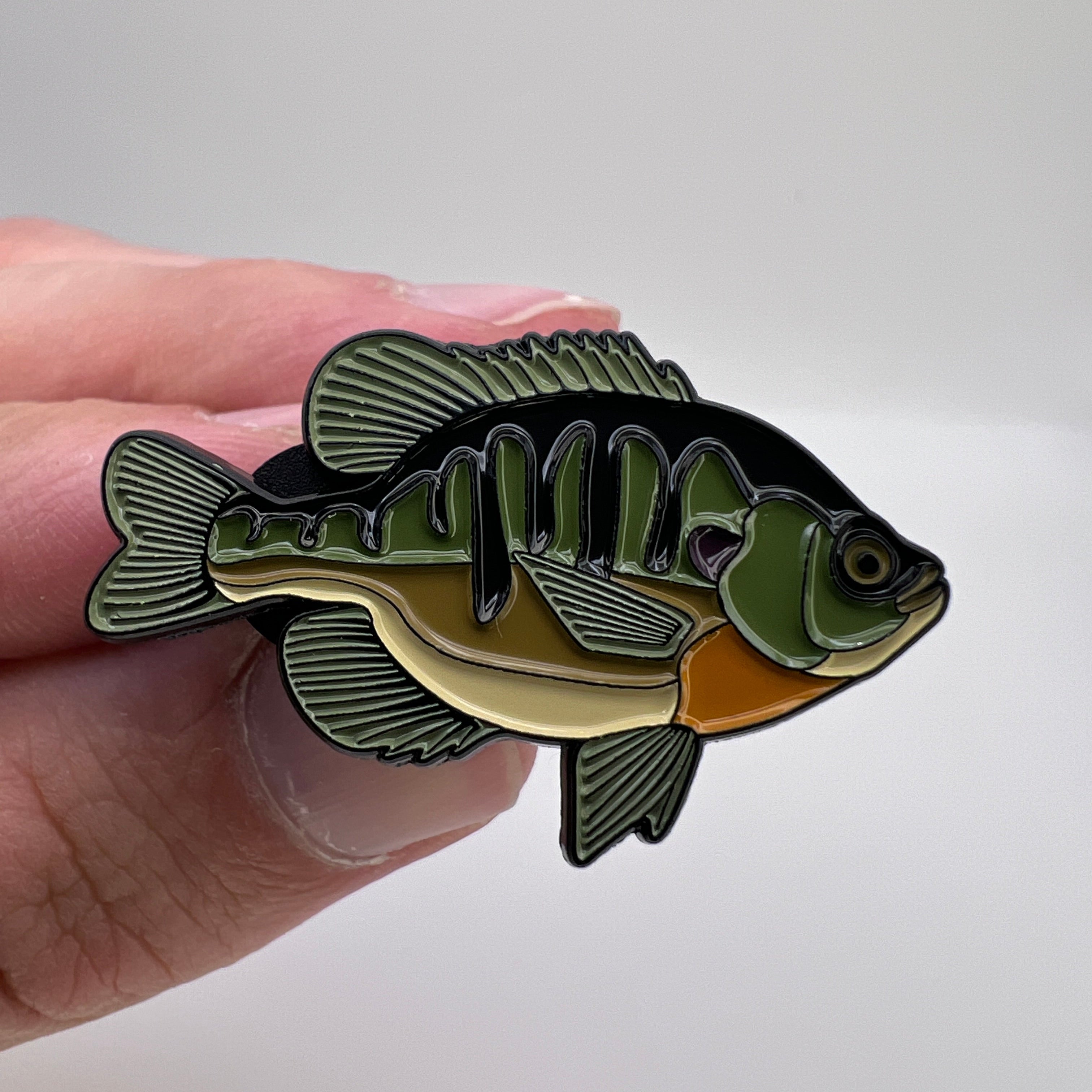 Fish-shaped pin held between fingers against a white background