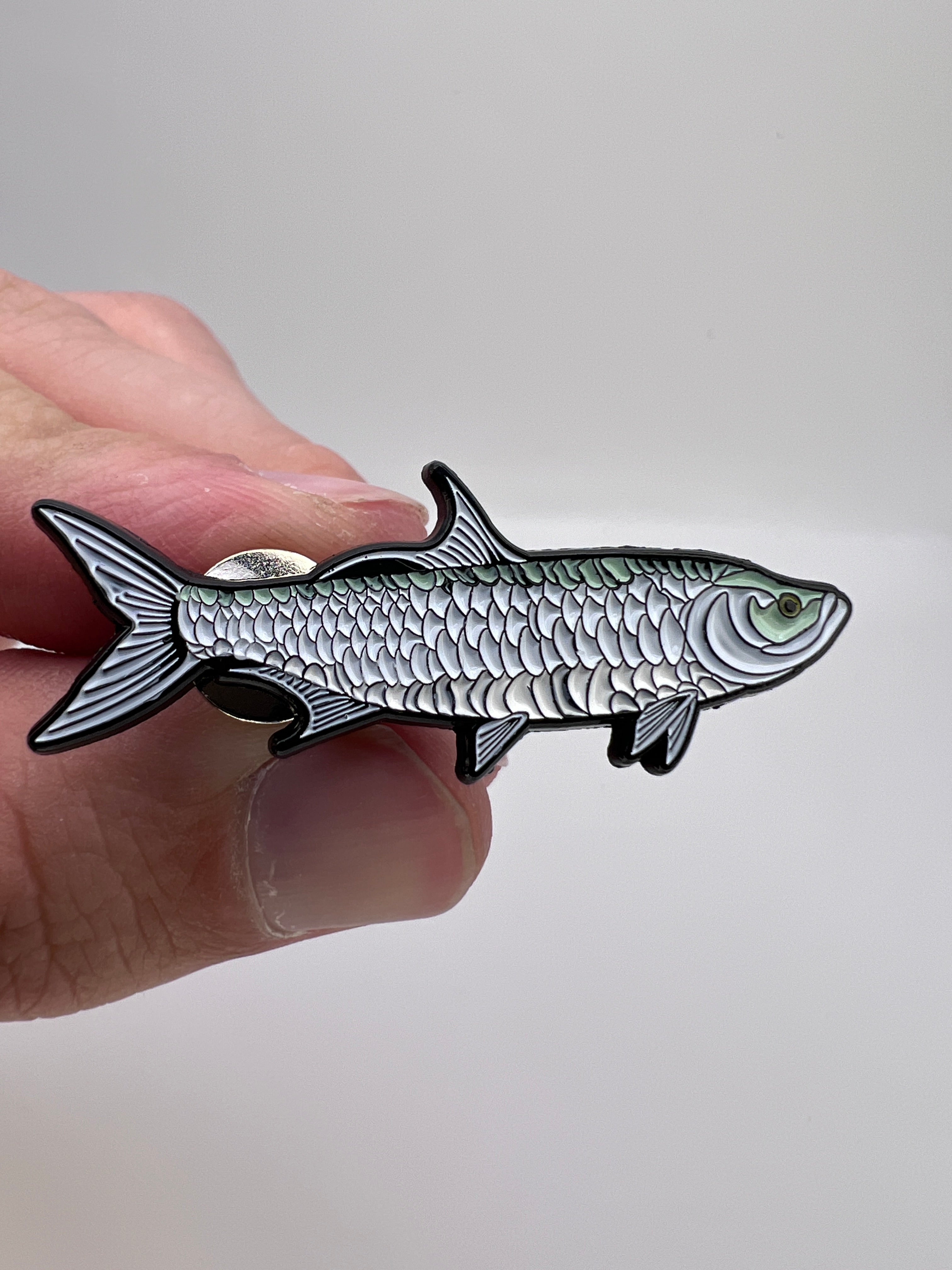 Fish-shaped pin held by a hand against a plain background