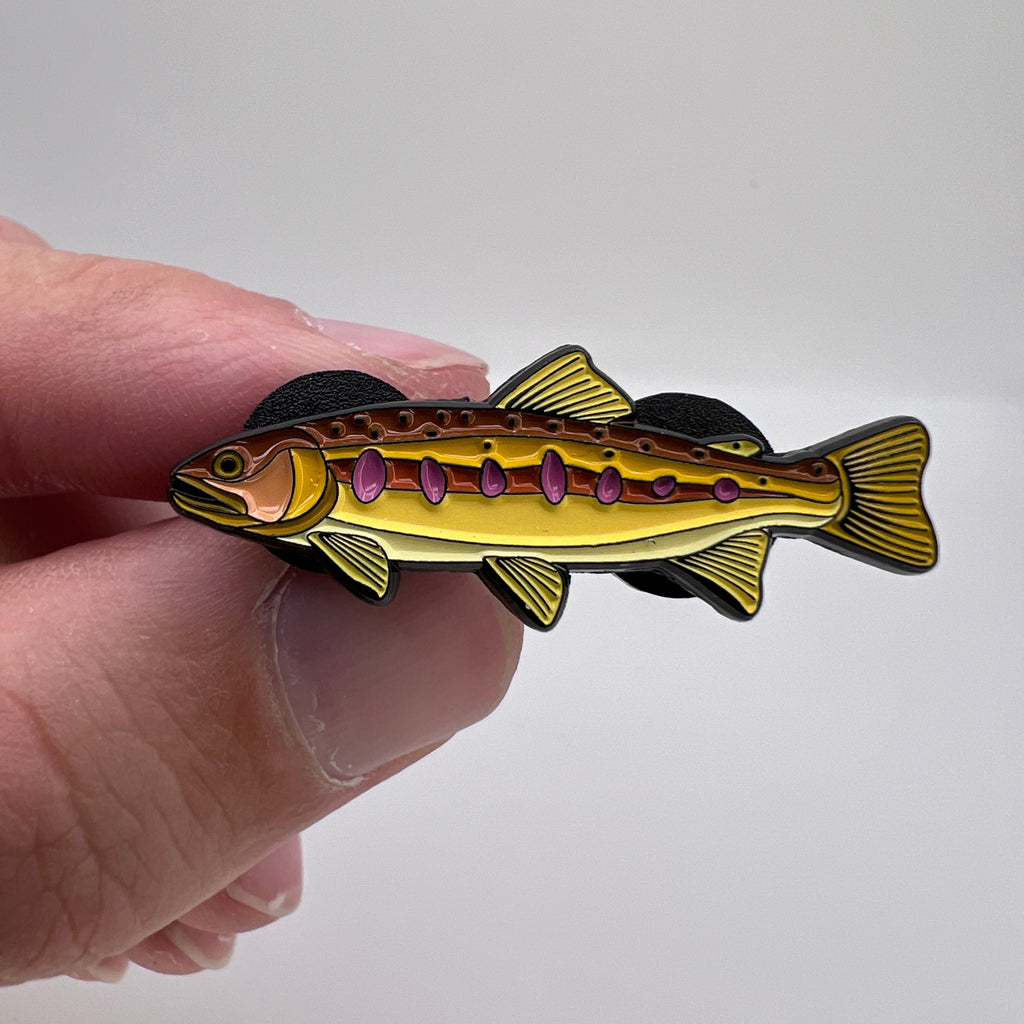 Hand holding a fish-shaped pin against a white background