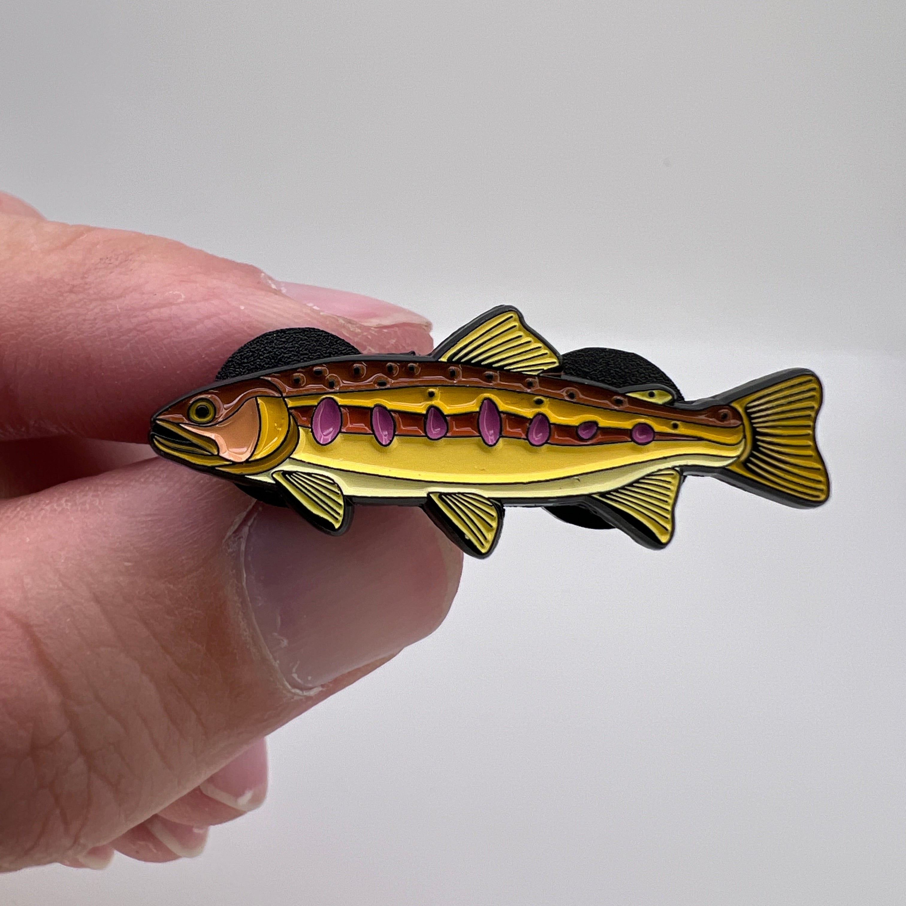 Hand holding a fish-shaped pin against a white background