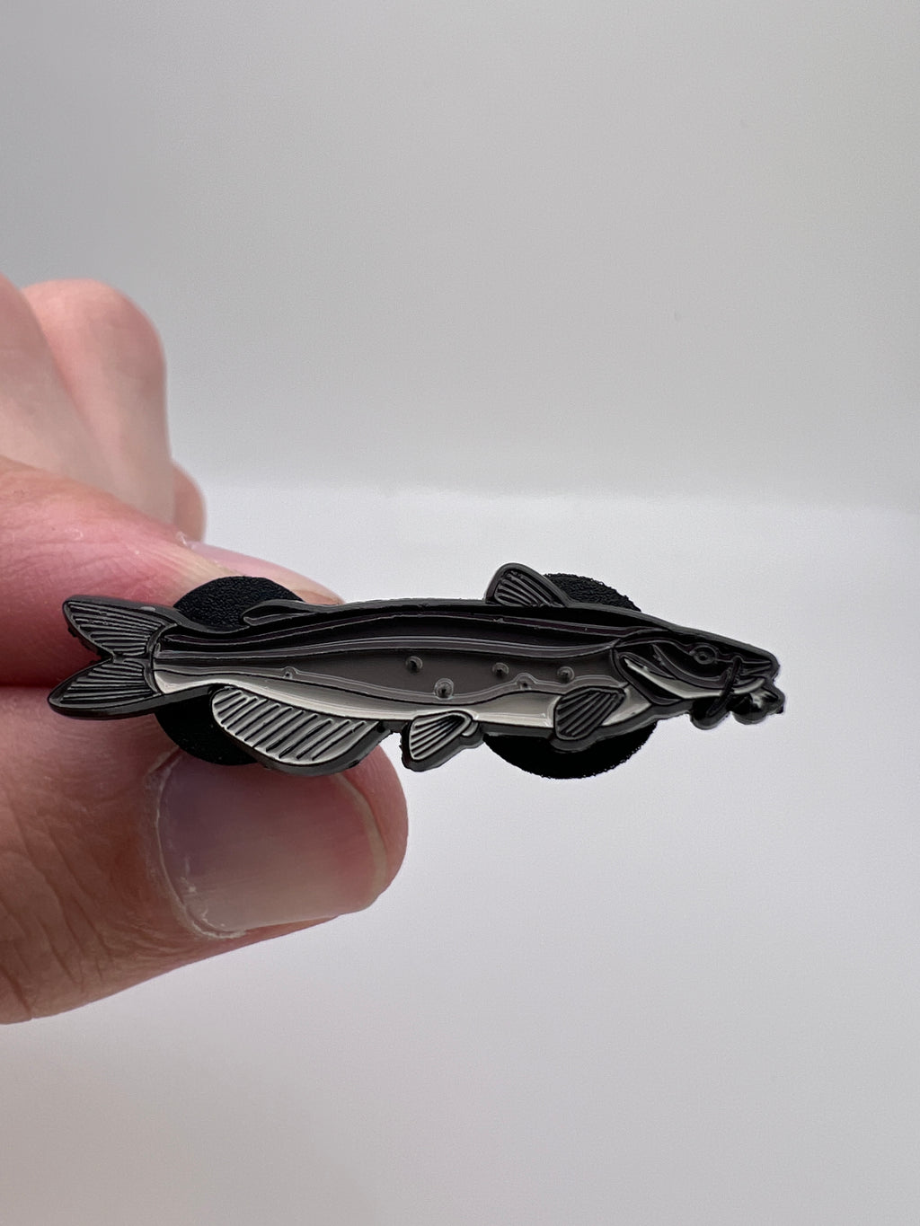 Hand holding a silver fish-shaped pin against a white background