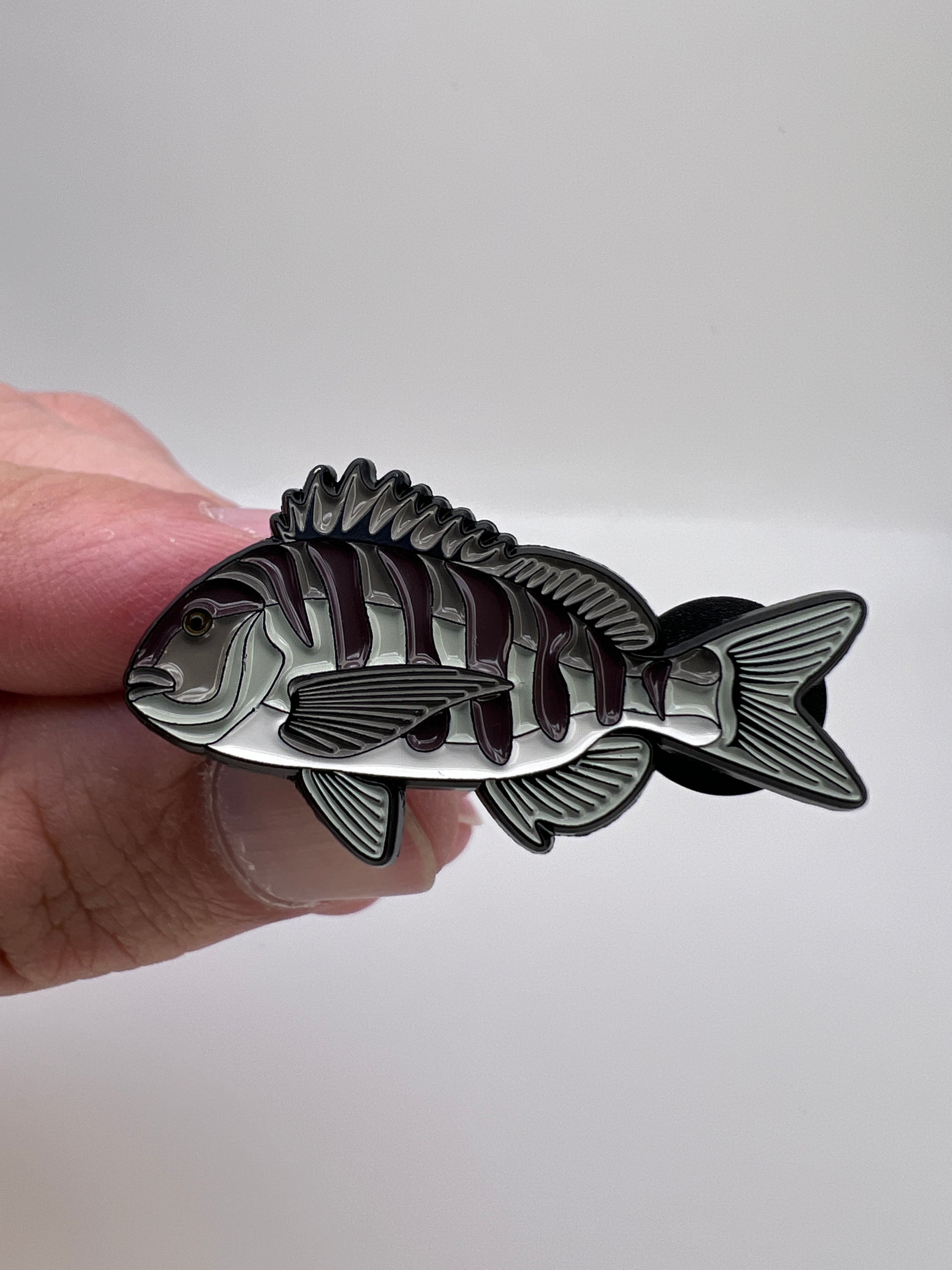 Hand holding a silver fish-shaped pin against a white background