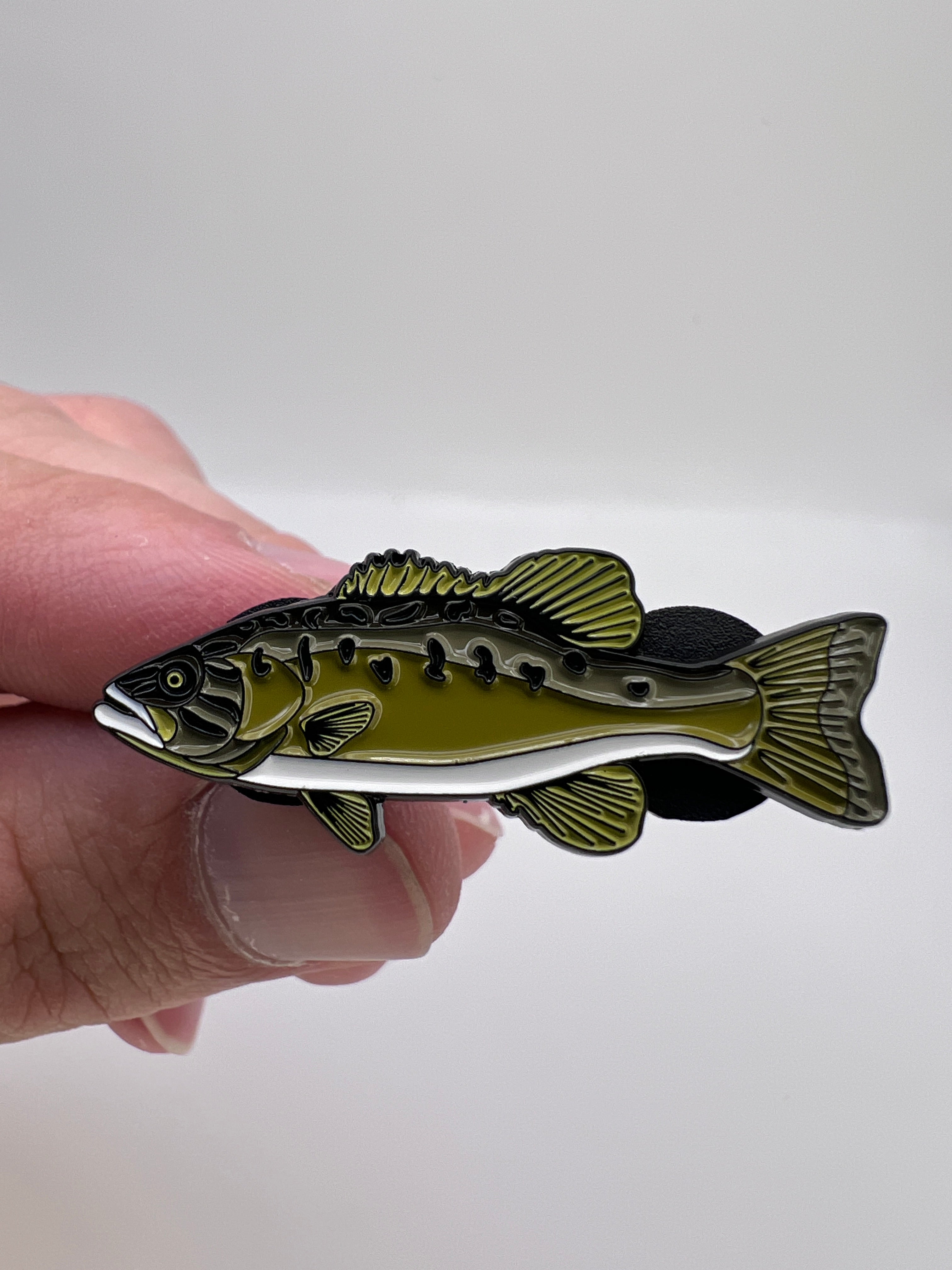 Hand holding a fish-shaped pin against a white background
