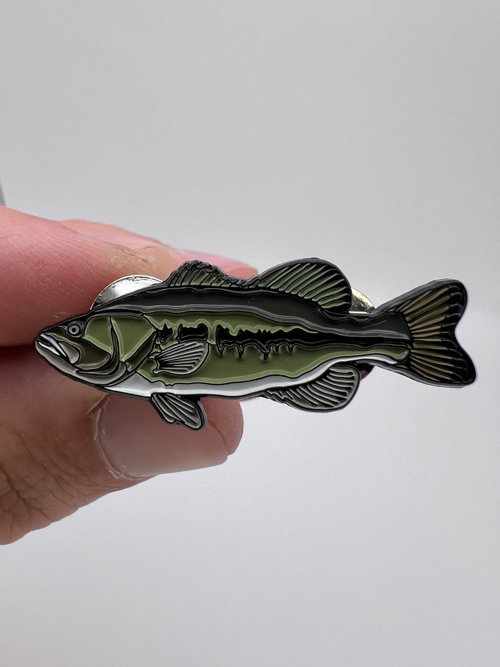 Fish-shaped metal badge held in a hand against a white background