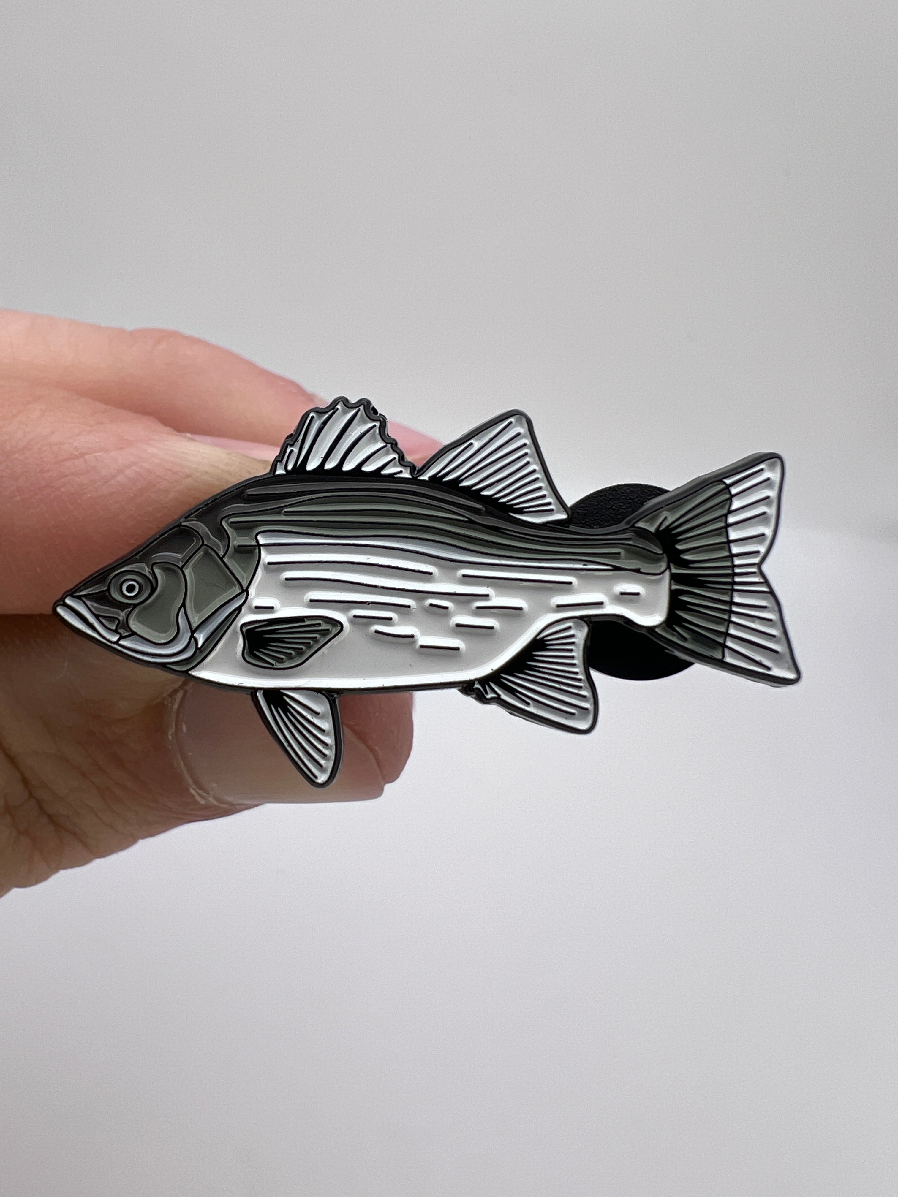 Fish-shaped metal badge held in a hand against a white background
