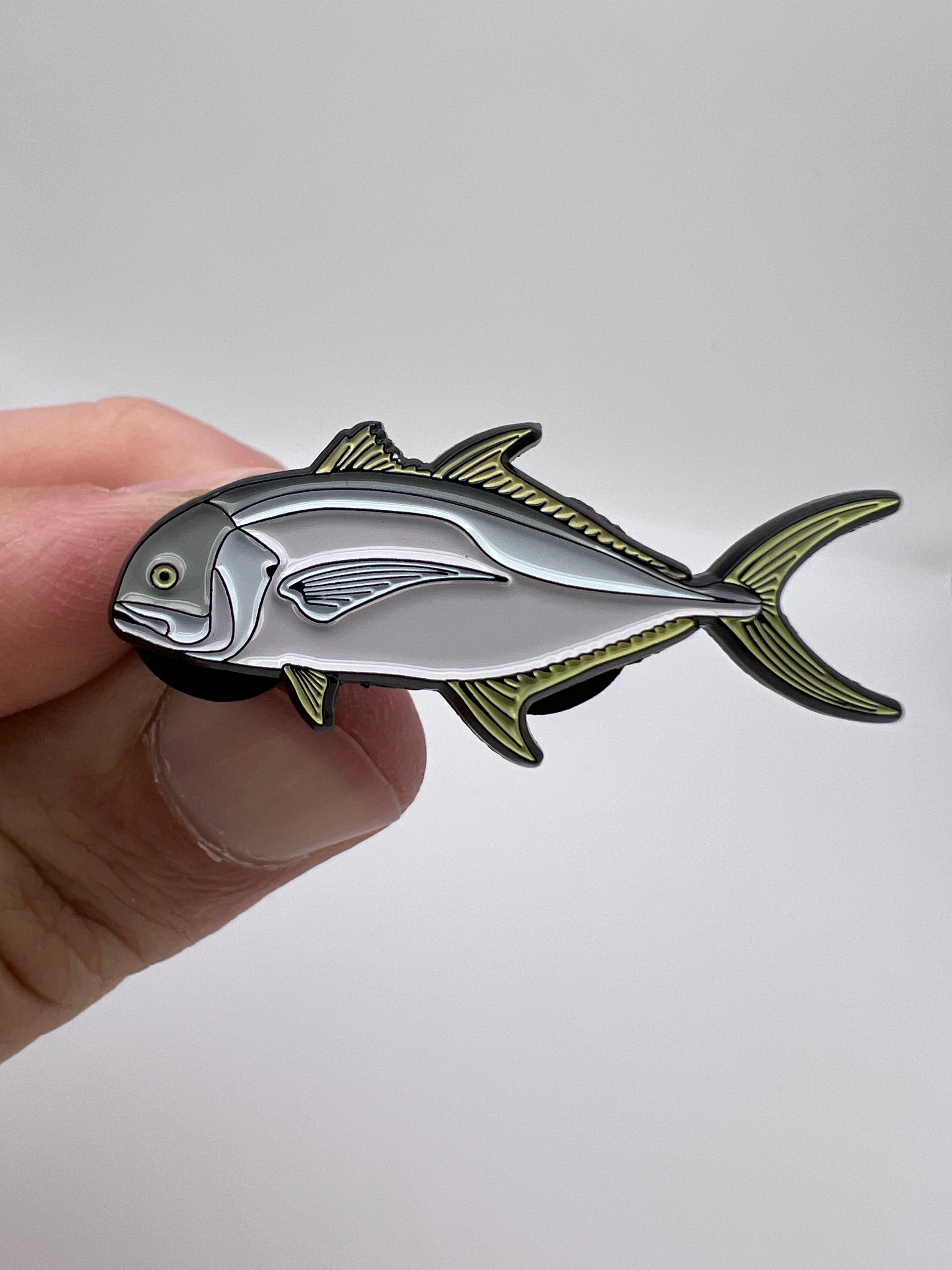 Fish-shaped metal badge held by a hand against a white background