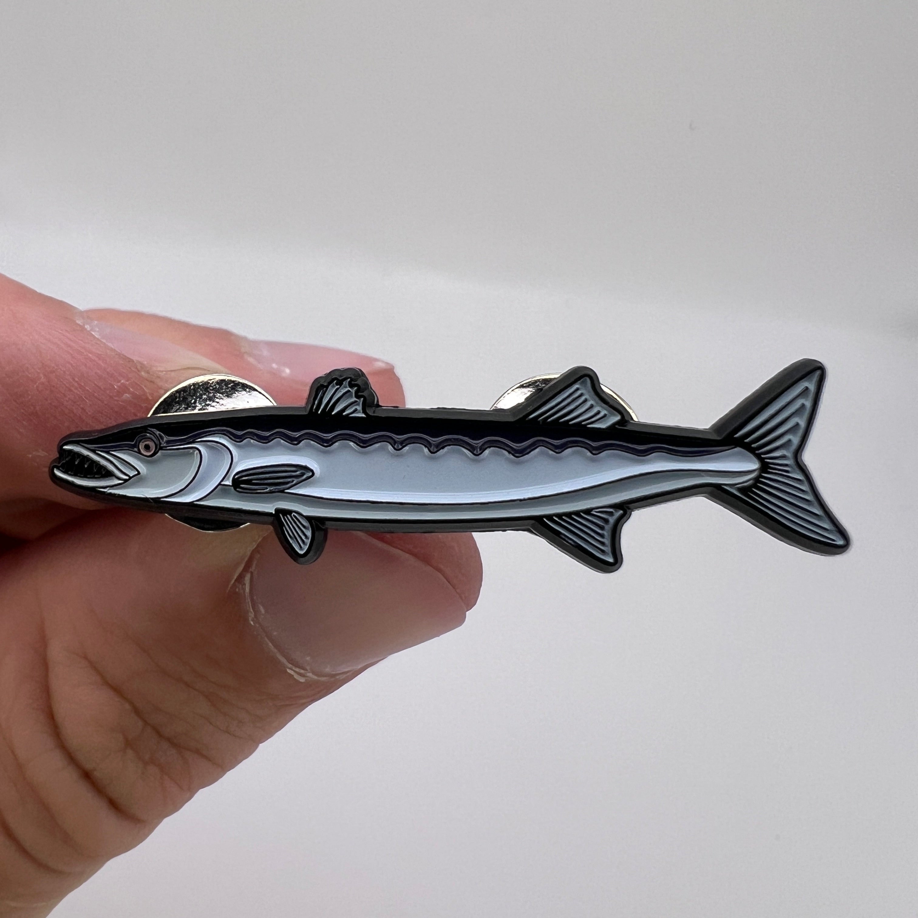 Hand holding a fish-shaped metal object against a white background