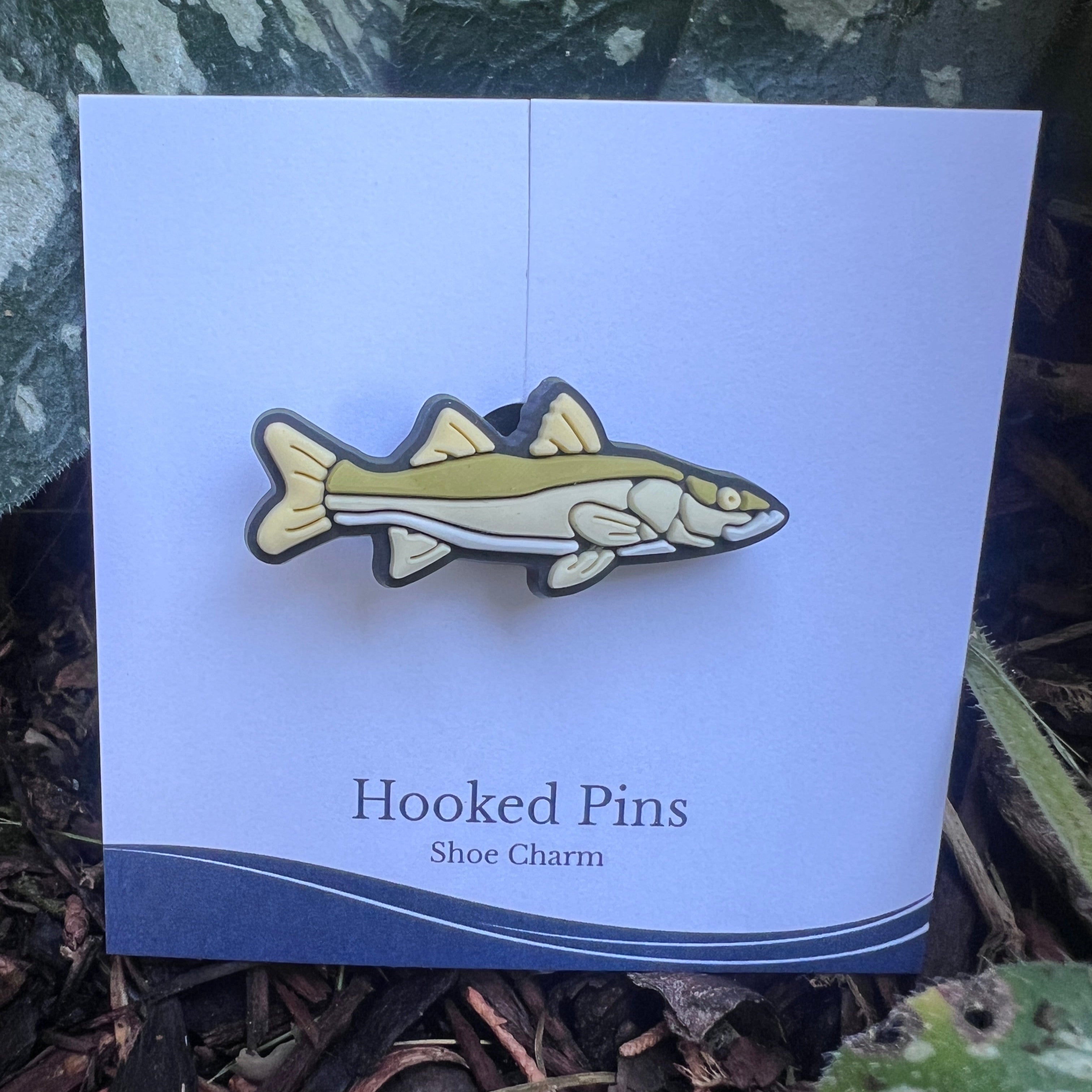 Fish-shaped shoe charm on a card labeled 'Hooked Pins' with a natural background