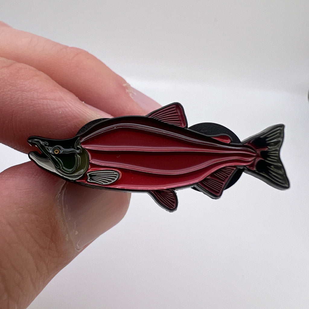 Salmon-shaped pin held between fingers against a white background