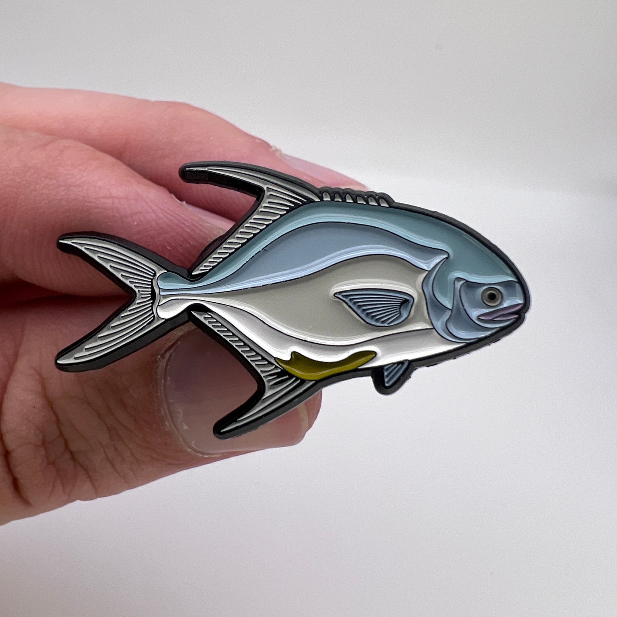 Fish-shaped pin held in a hand against a white background