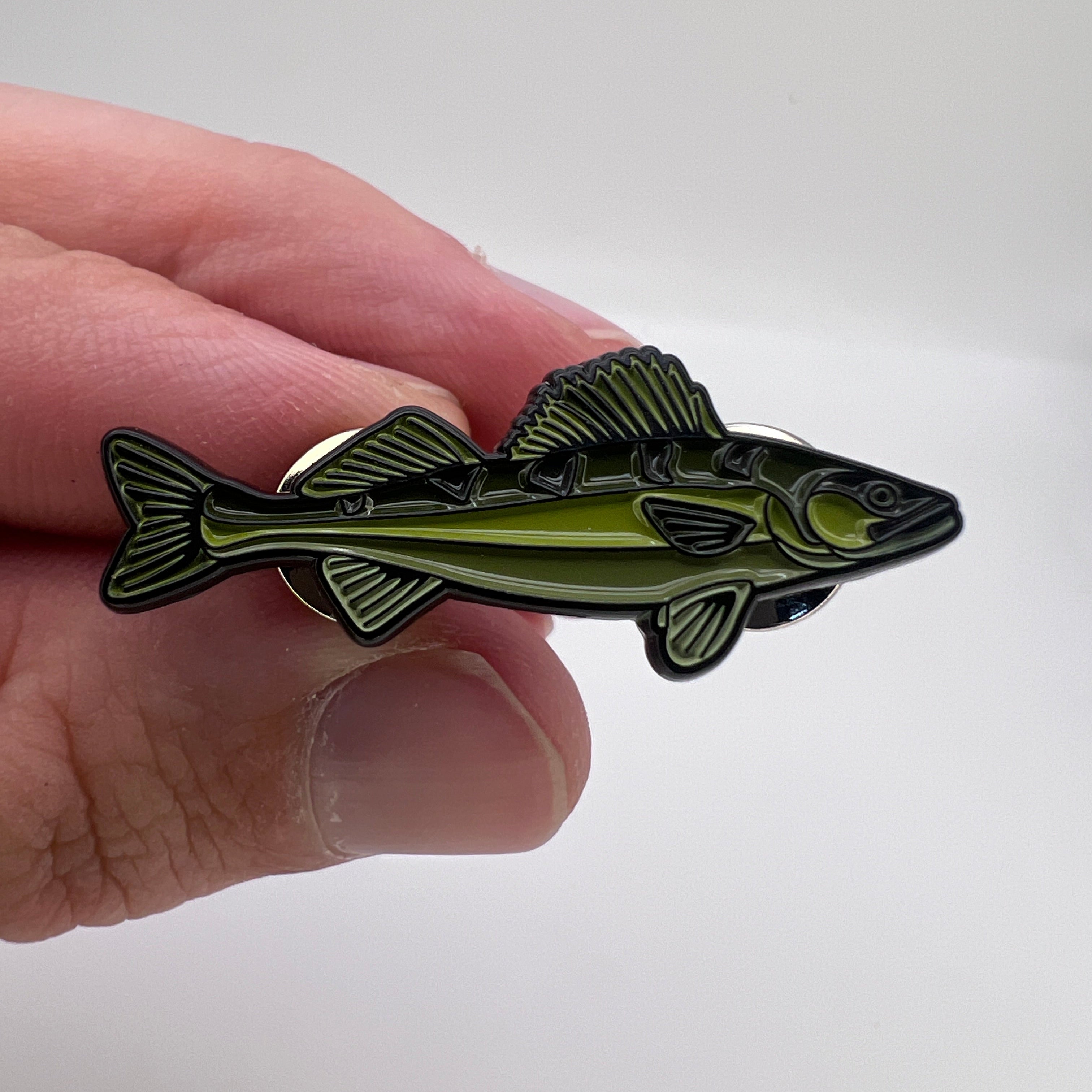Hand holding a fish-shaped pin against a white background